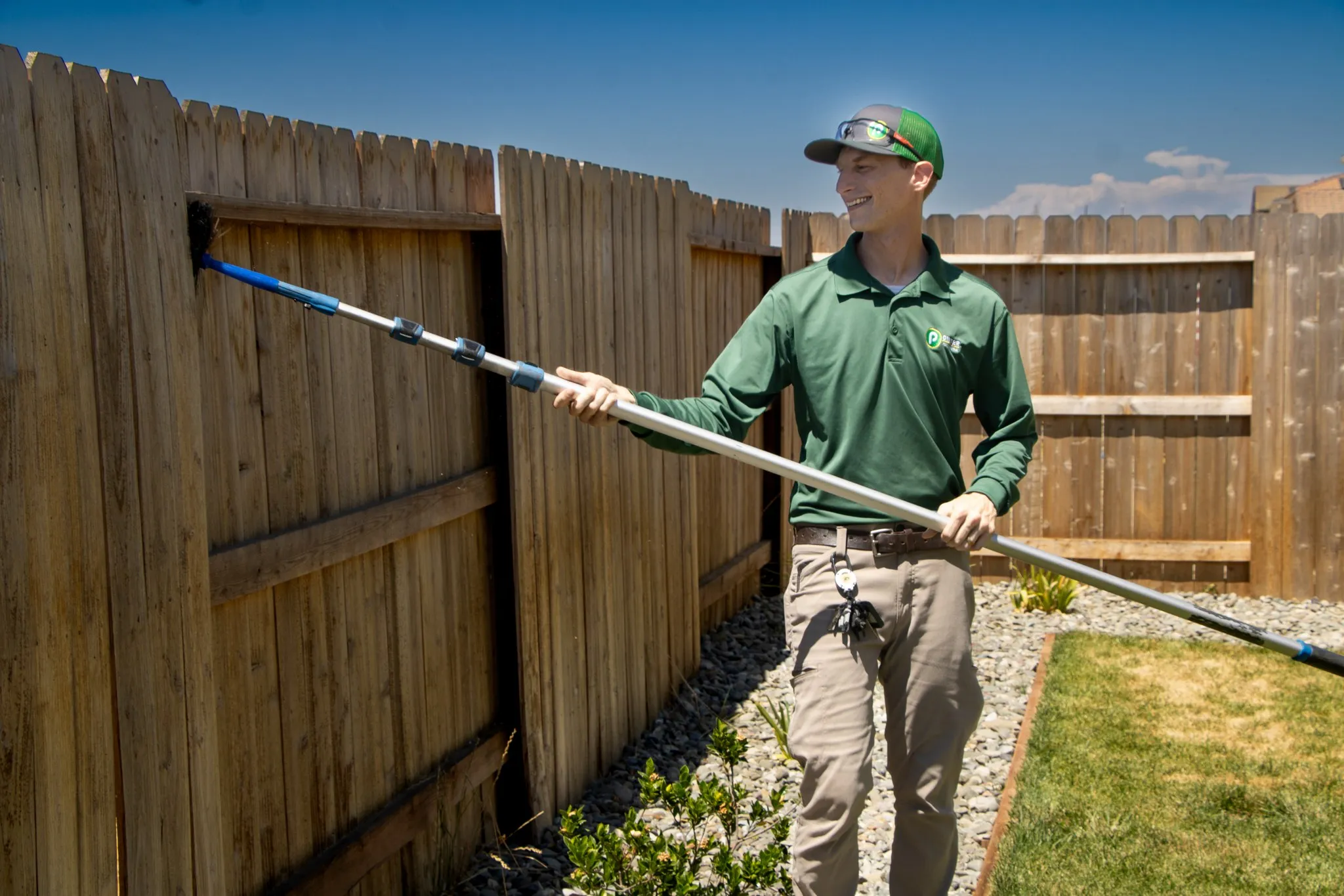 Pointer Pest Control technician removing spider webs along a backyard fence line at a Granite Bay CA estate